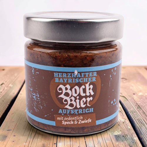Glas Bockbier-Aufstrich mit Speck und Zwiebel, braunes Etikett mit hellblauen Streifen, auf einem Holztisch.