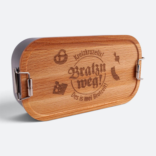 Brotzeitbox mit Buchenholzdeckel und der Gravur „Kreizkruzefix! Bratzn weg! Des is mei Brotzeit!“ mit Brezn, Käse, Radi und Wurst.