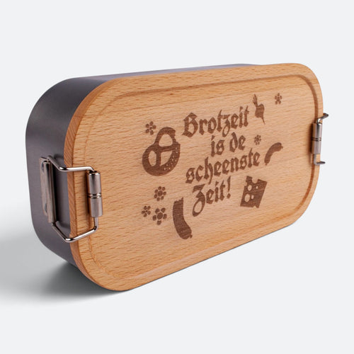 Brotzeitbox aus Edelstahl mit Buchenholzdeckel und der Gravur „Brotzeit is de scheenste Zeit!“ mit Brezn, Wurst, Radi und Käse.