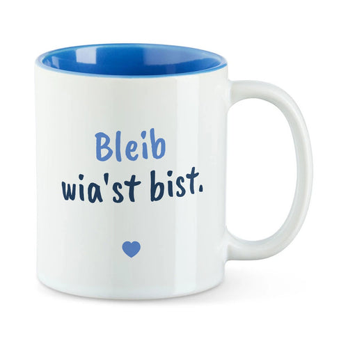 Weiße Tasse mit blauer Innenseite und dem bairischen Spruch „Bleib wia'st bist.“ in Pinselschrift.