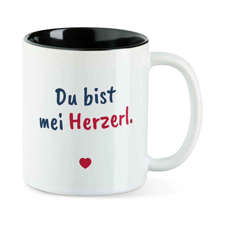 Weiße Tasse mit schwarzer Innenseite und dem bairischen Spruch „Du bist mei Herzerl.“ in Pinselschrift.
