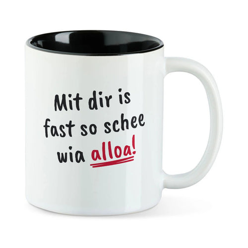 Weiße Tasse mit schwarzer Innenseite und dem bairischen Spruch „Mit dir is fast so schee wia alloa!“ in Pinselschrift.