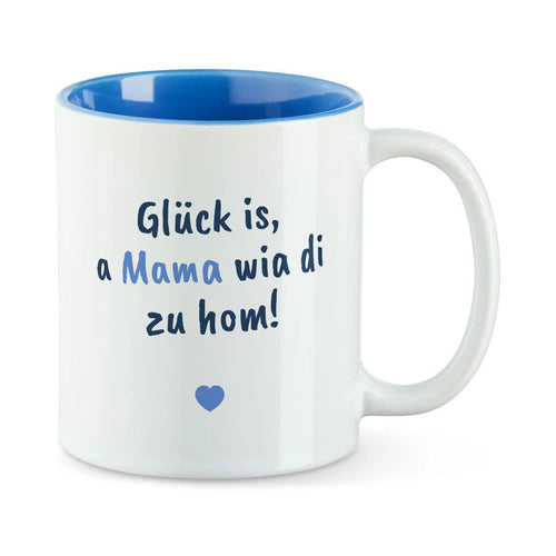 Weiße Tasse mit blauer Innenseite und dem bairischen Spruch „Glück is, a Mama wia di zu hom!“ in Pinselschrift.