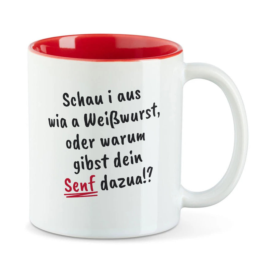 Weiße Tasse mit roter Innenseite und dem bairischen Spruch „Schau i aus wia a Weißwurst, oder warum gibst dein Senf dazua!?“ in Pinselschrift.