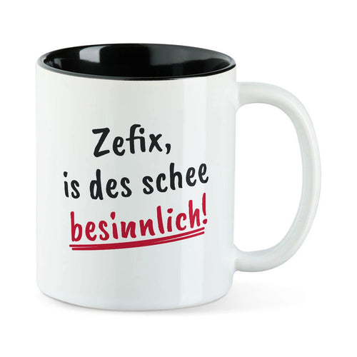 Weiße Tasse mit schwarzer Innenseite und dem bairischen Spruch „Zefix, is des schee besinnlich!“ in Pinselschrift.