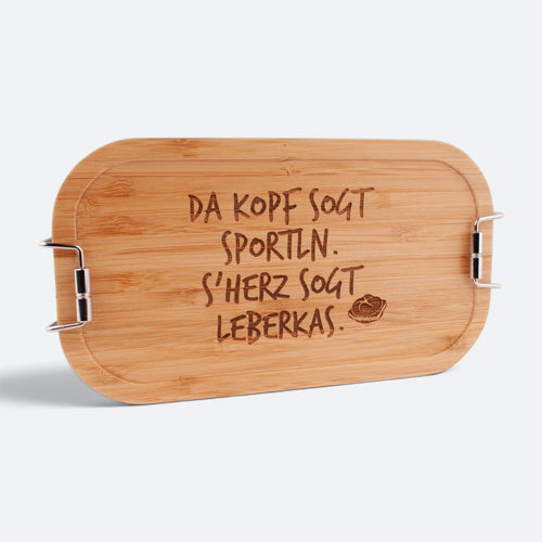 Brotzeitbox mit Bambusdeckel und der Gravur „Da Kopf sogt Sportln. S'Herz sogt Leberkas.“ mit Leberkassemmel.