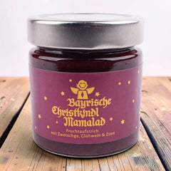Glas Bayrische Christkindl Mamalad, Fruchtaufstrich mit Zwetschge, Glühwein und Zimt, lila Etikett mit goldenem Engel und Sternen, auf einem Holztisch.