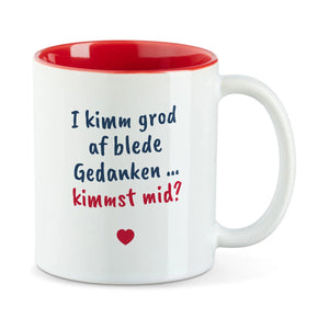 Weiße Tasse mit roter Innenseite und dem bairischen Spruch „I kimm grod af blede Gedanken … kimmst mid?“ in Pinselschrift.