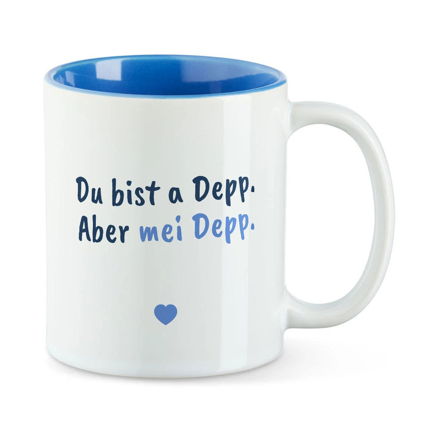Weiße Tasse mit blauer Innenseite und dem bairischen Spruch „Du bist a Depp. Aber mei Depp.“ in Pinselschrift.
