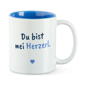 Weiße Tasse mit blauer Innenseite und dem bairischen Spruch „Du bist mei Herzerl.“ in Pinselschrift.