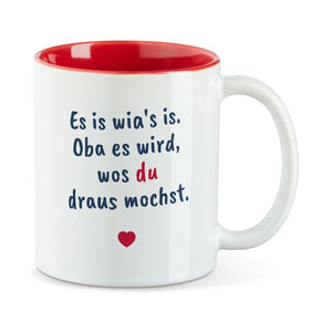 Weiße Tasse mit roter Innenseite und dem bairischen Spruch „Es is wia's is. Oba es wird, wos du draus mochst.“ in Pinselschrift.
