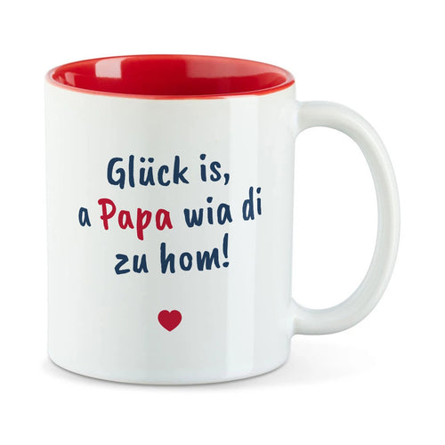 Weiße Tasse mit roter Innenseite und dem bairischen Spruch „Glück is, a Papa wia di zu hom!“ in Pinselschrift.