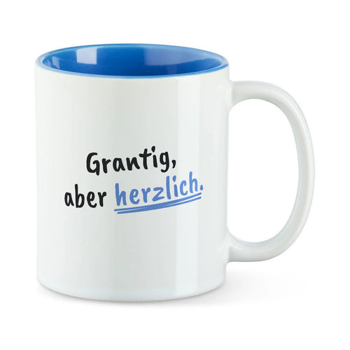 Weiße Tasse mit blauer Innenseite und dem bairischen Spruch „Grantig, aber herzlich.“ in Pinselschrift.