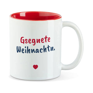 Weiße Tasse mit roter Innenseite und dem bairischen Spruch „Gsegnete Weihnachtn.“ in Pinselschrift.