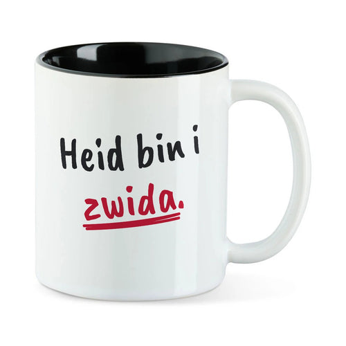 Weiße Tasse mit schwarzer Innenseite und dem bairischen Spruch „Heid bin i zwida.“ in Pinselschrift.