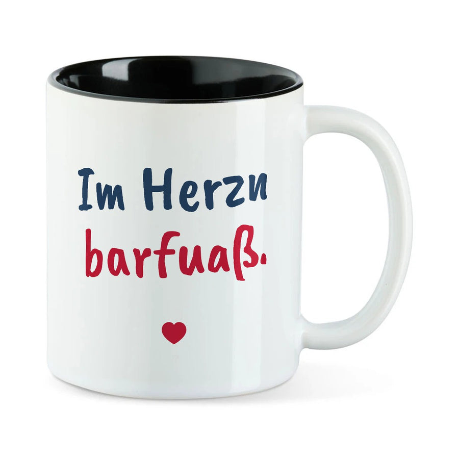 Weiße Tasse mit schwarzer Innenseite und dem bairischen Spruch „Im Herzn barfuaß.“ in Pinselschrift.