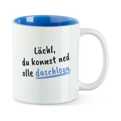 Weiße Tasse mit blauer Innenseite und dem bairischen Spruch „Lächl, du konnst ned olle daschlogn.“ in Pinselschrift.