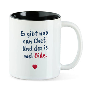 Weiße Tasse mit schwarzer Innenseite und dem bairischen Spruch „Es gibt nua oan Chef. Und des is mei Oide.“ in Pinselschrift.