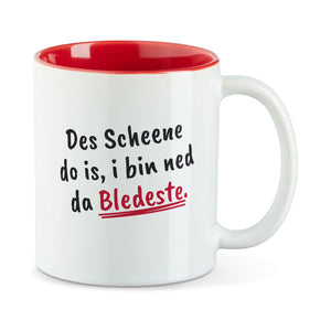 Weiße Tasse mit roter Innenseite und dem bairischen Spruch „Des Scheene do is, i bin ned da Bledeste.“ in Pinselschrift.
