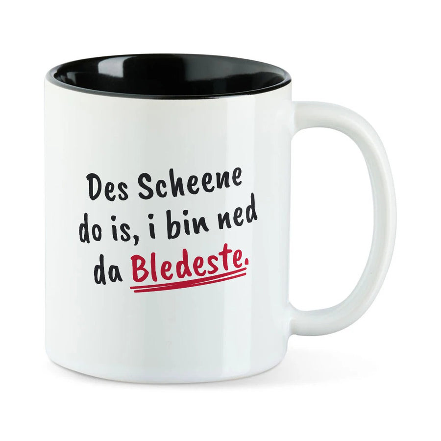 Weiße Tasse mit schwarzer Innenseite und dem bairischen Spruch „Des Scheene do is, i bin ned da Bledeste.“ in Pinselschrift.