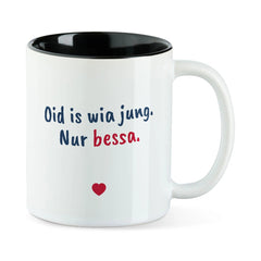 Weiße Tasse mit schwarzer Innenseite und dem bairischen Spruch „Oid is wia jung. Nur bessa.“ in Pinselschrift.