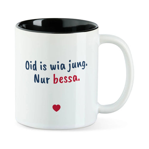 Weiße Tasse mit schwarzer Innenseite und dem bairischen Spruch „Oid is wia jung. Nur bessa.“ in Pinselschrift.