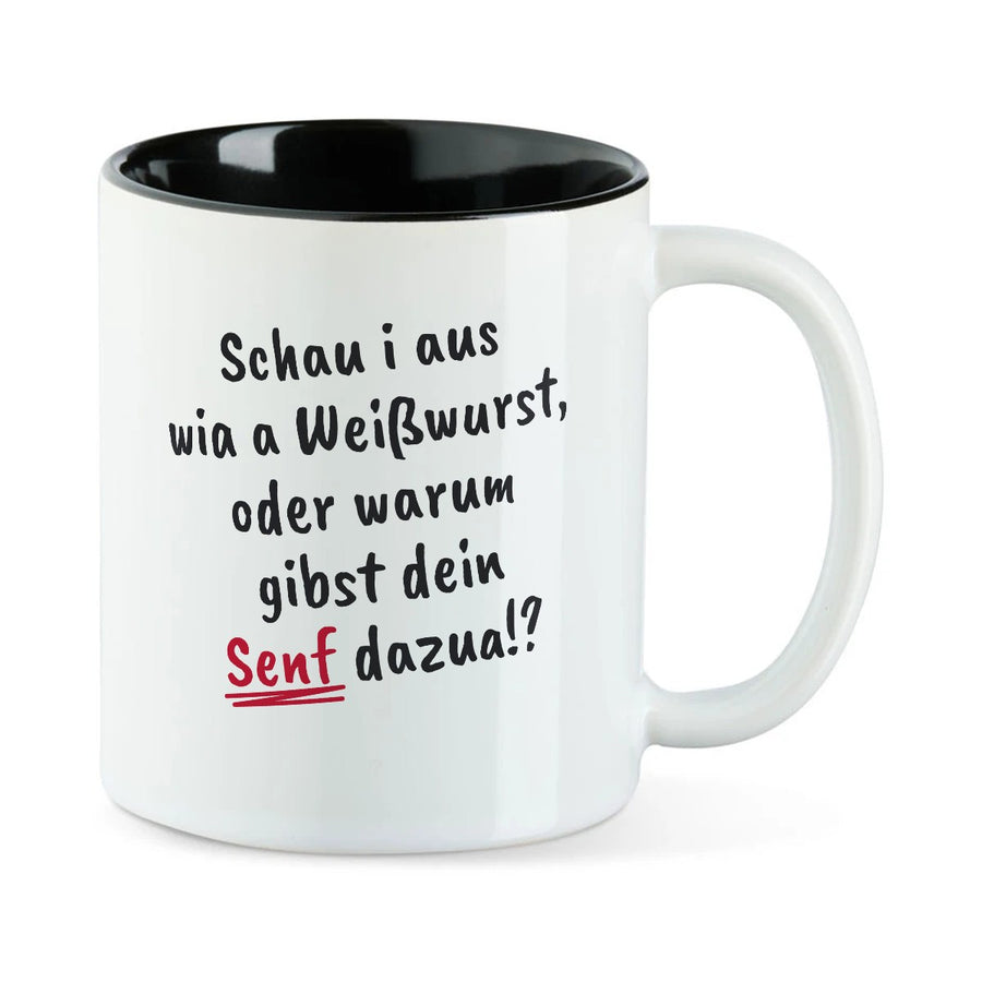 Weiße Tasse mit schwarzer Innenseite und dem bairischen Spruch „Schau i aus wia a Weißwurst, oder warum gibst dein Senf dazua!?“ in Pinselschrift.