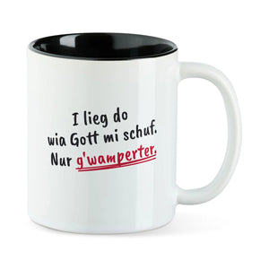 Weiße Tasse mit schwarzer Innenseite und dem bairischen Spruch „I lieg do wia Gott mi schuf. Nur g'wamperter.“ in Pinselschrift.